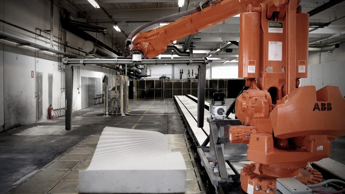 Industrial robot with a hot-wire cutting frame above shaped foam in a fabrication workshop.