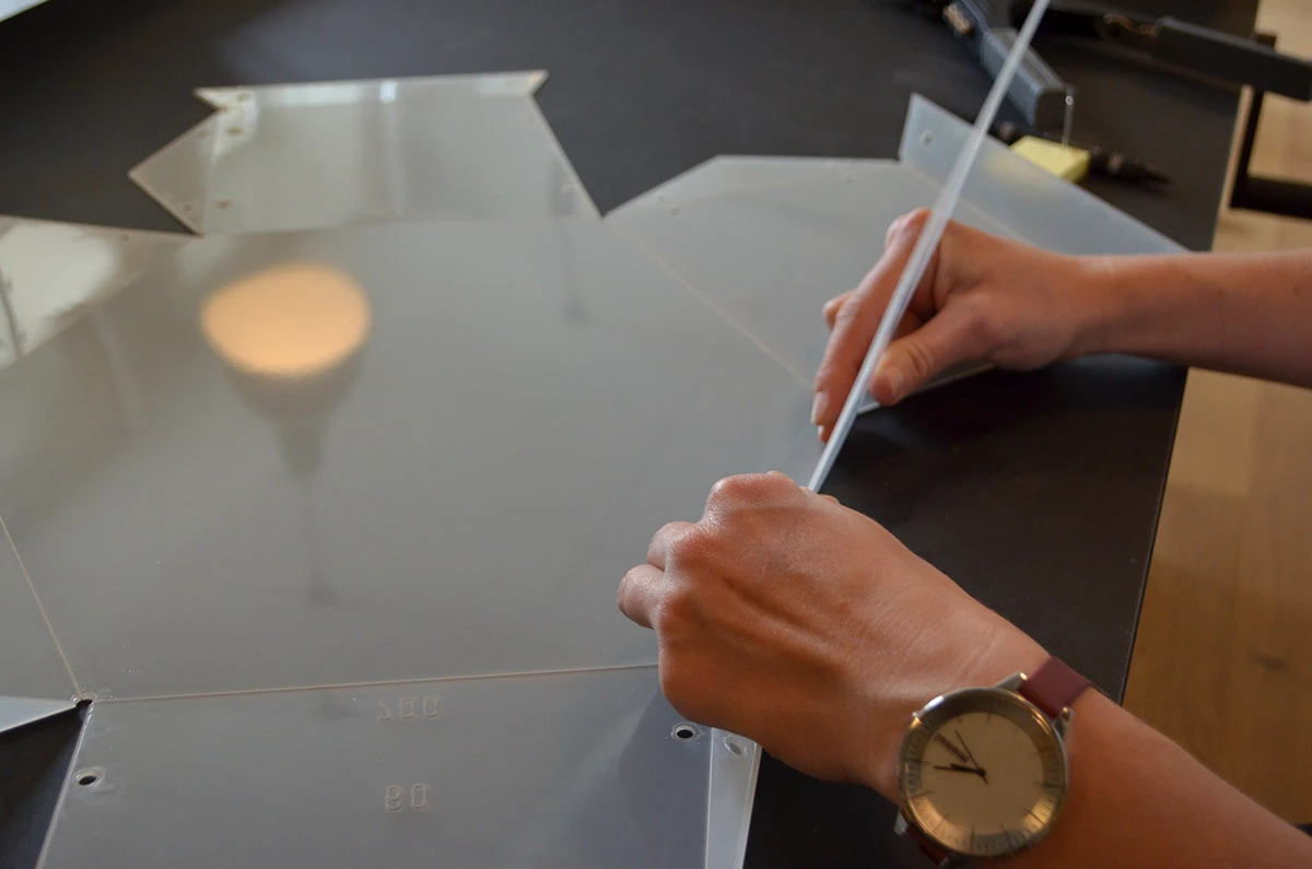 Hands folding a scored polypropylene sheet during fabrication.